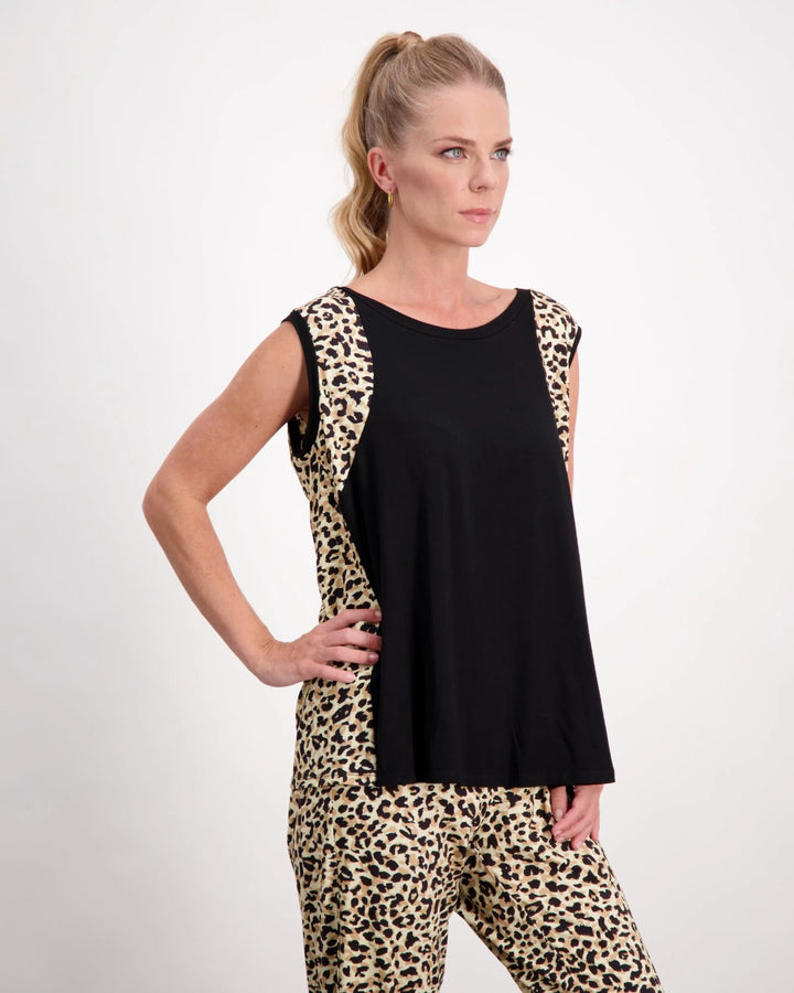 ?A standing blonde female with blue eyes wearing a pony-tail is wearing a black and leopard print bamboo sleeveless physio top. The leopard print highlights the black front of the top. She has paired the top with matching leopard print bamboo pants. Christina Stephens Australian Adaptive Clothing.